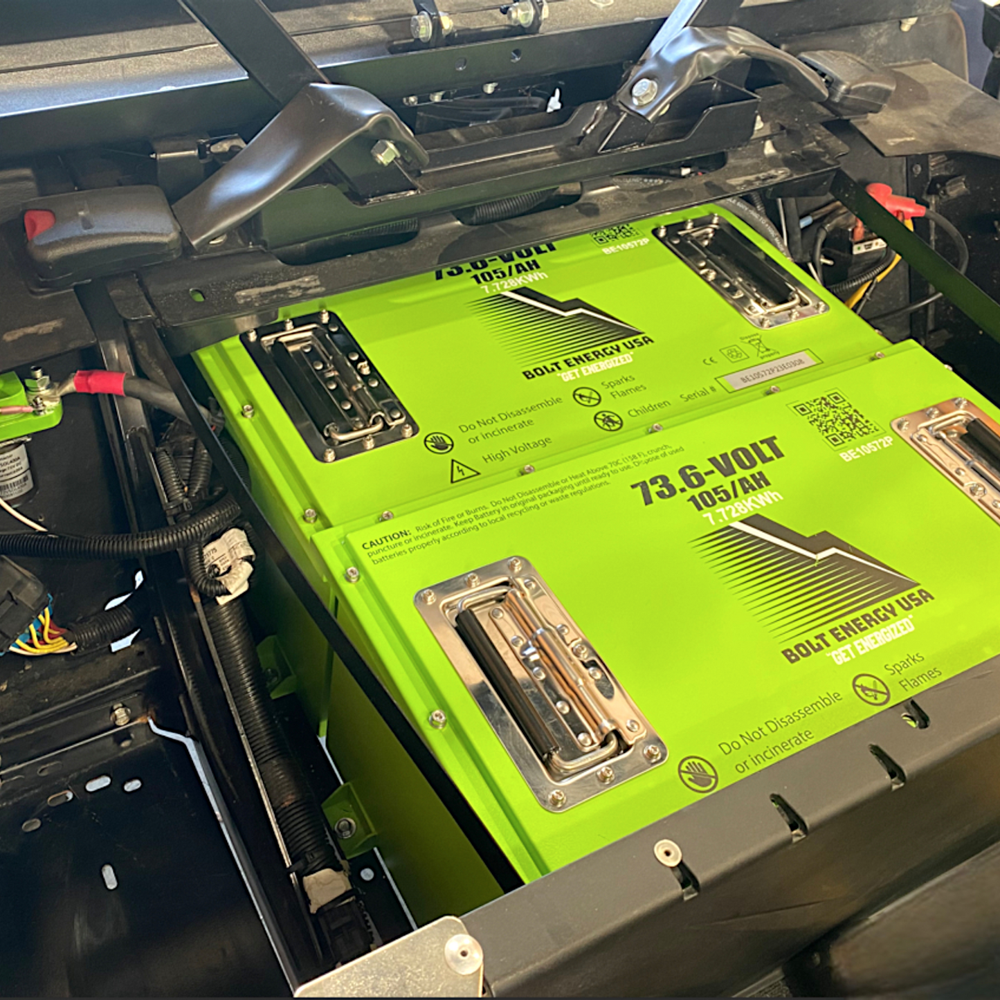 Two green Bolt Energy USA lithium batteries installed under a vehicle seat, showing 73.6-Volt, 105AH, and 7.728KWh specifications.