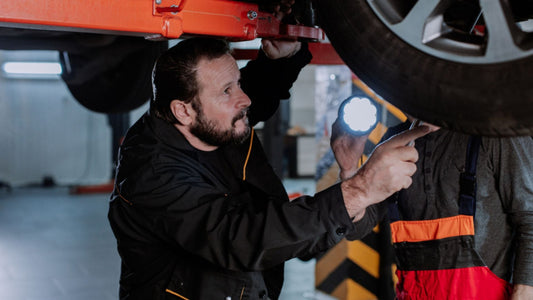 Mechanic inspecting Bad Boy buggy axle assembly with flashlight under vehicle, demonstrating diagnostic techniques for identifying and repairing strange noises from axle components.